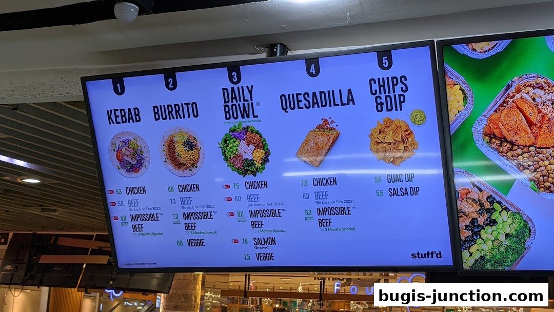 A digital menu board displaying various food items like kebabs, burritos, bowls, quesadillas, and chips with dips.