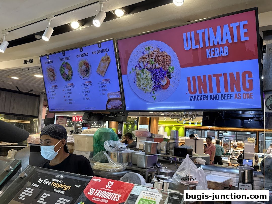 A food stall display with digital menus showing kebabs, bowls, burritos, and quesadillas.