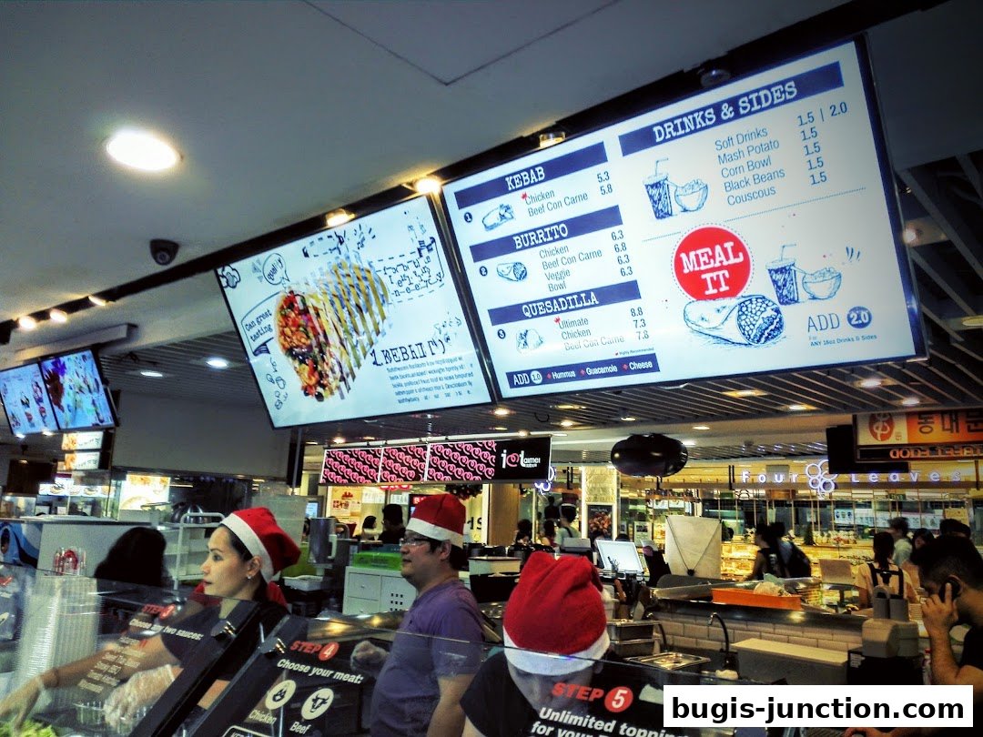 A brightly lit food counter with digital menus displaying kebabs, burritos, quesadillas, and drinks.