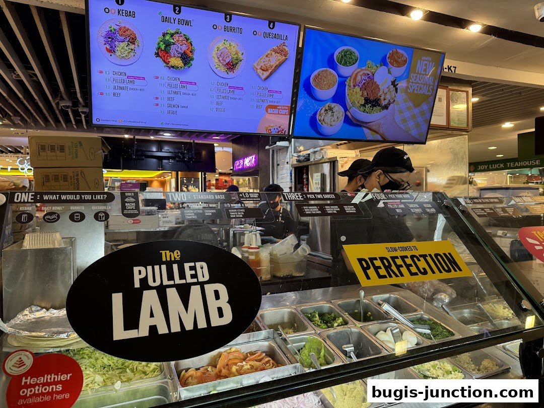 A food counter displaying various meal options and ingredients, with digital menus above.