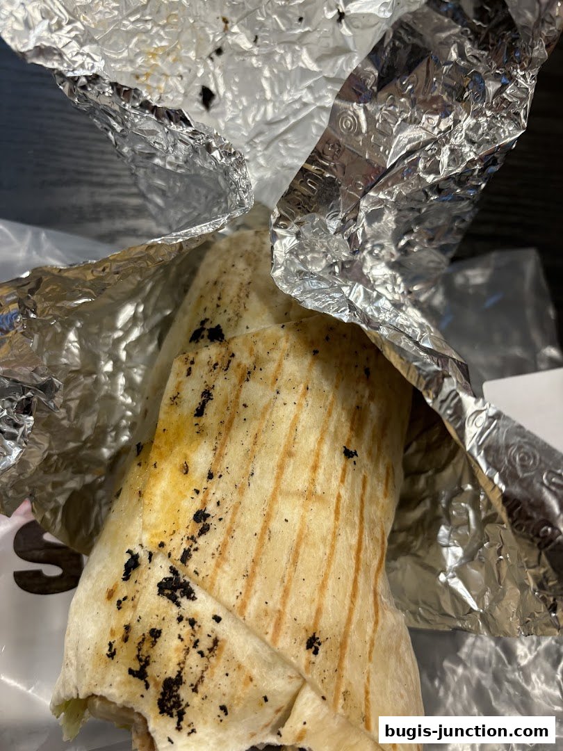 A close-up shot of a grilled wrap, partially unwrapped from foil.