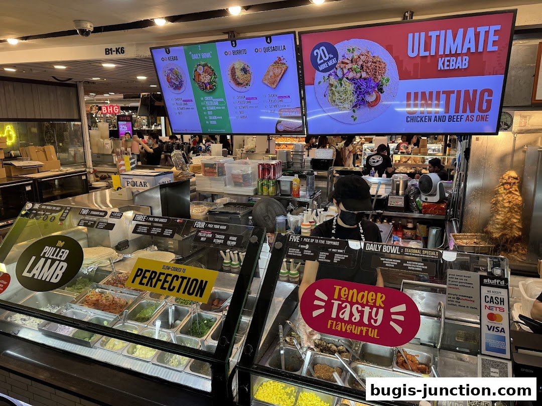 A food stall with a display of ingredients and a large screen showing menu items.