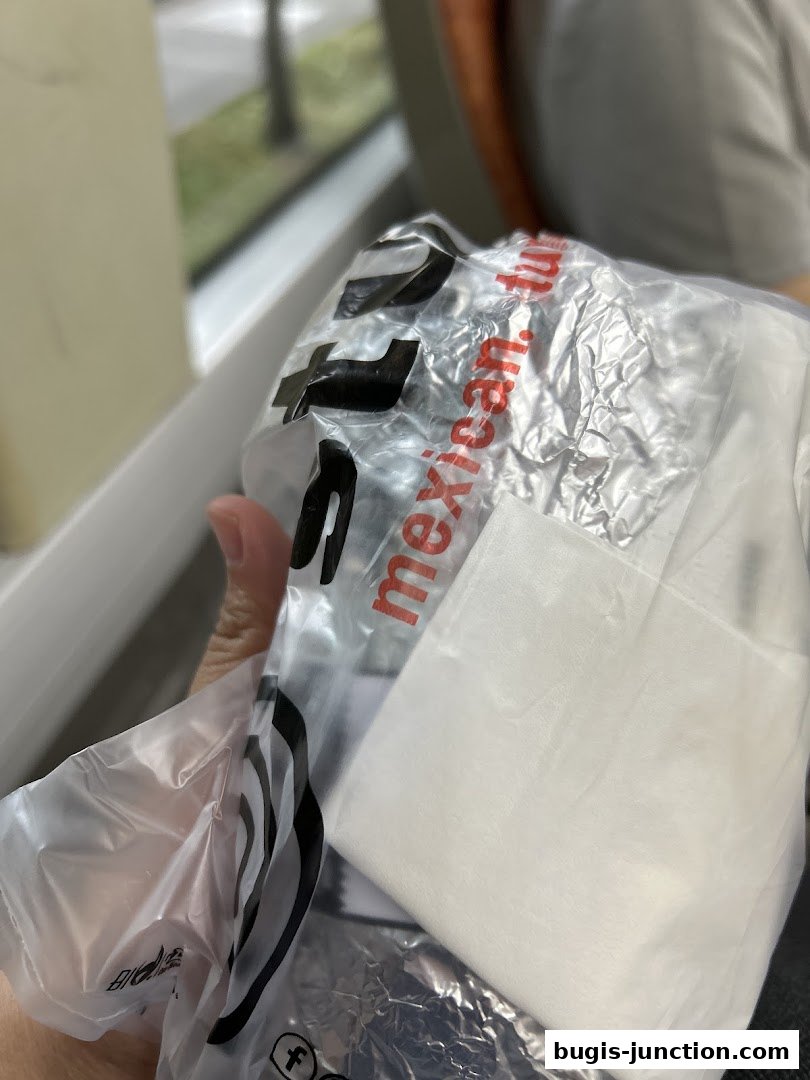 A person holds a plastic bag with a Mexican food logo and a white napkin.