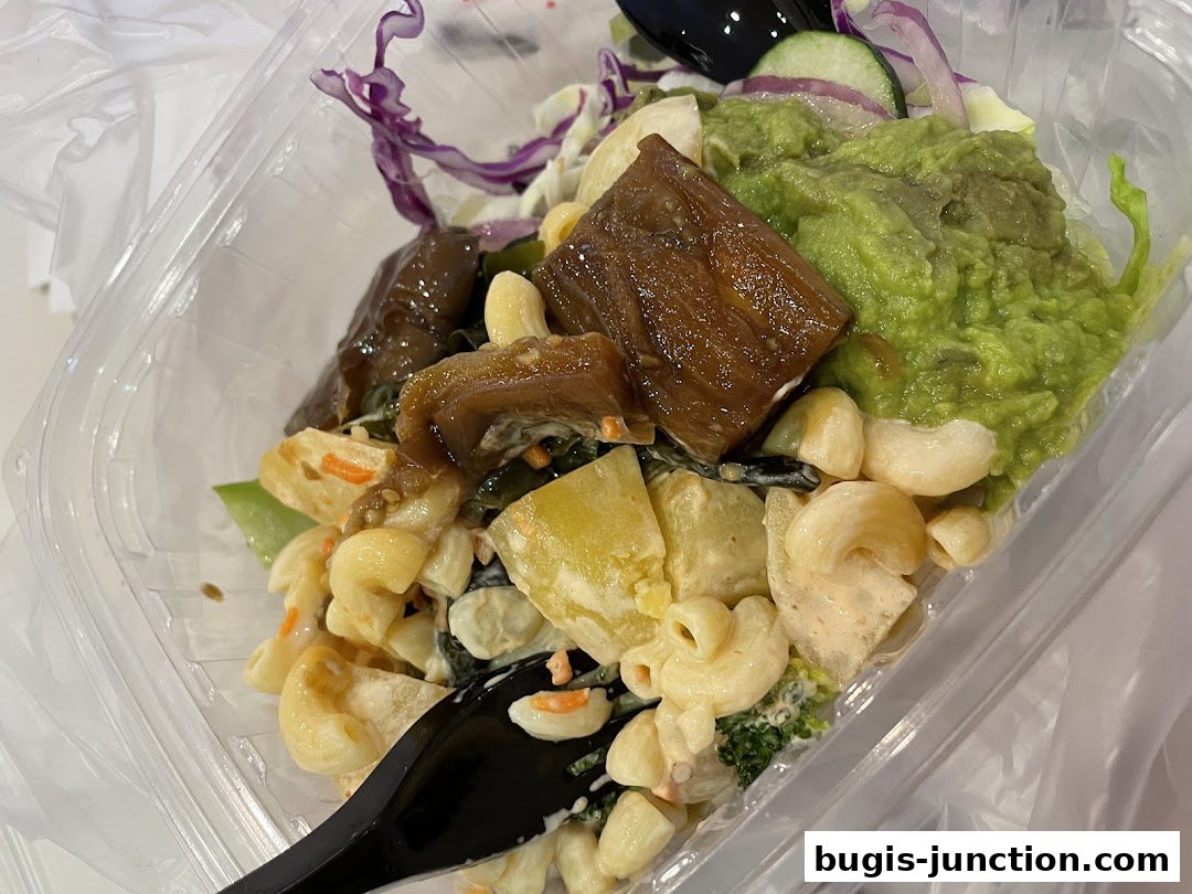 A close-up of a takeaway salad with pasta, avocado, and meat.