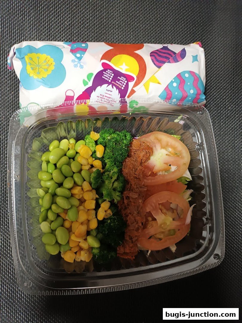 A clear plastic container filled with a healthy salad featuring edamame, corn, broccoli, and tomatoes.