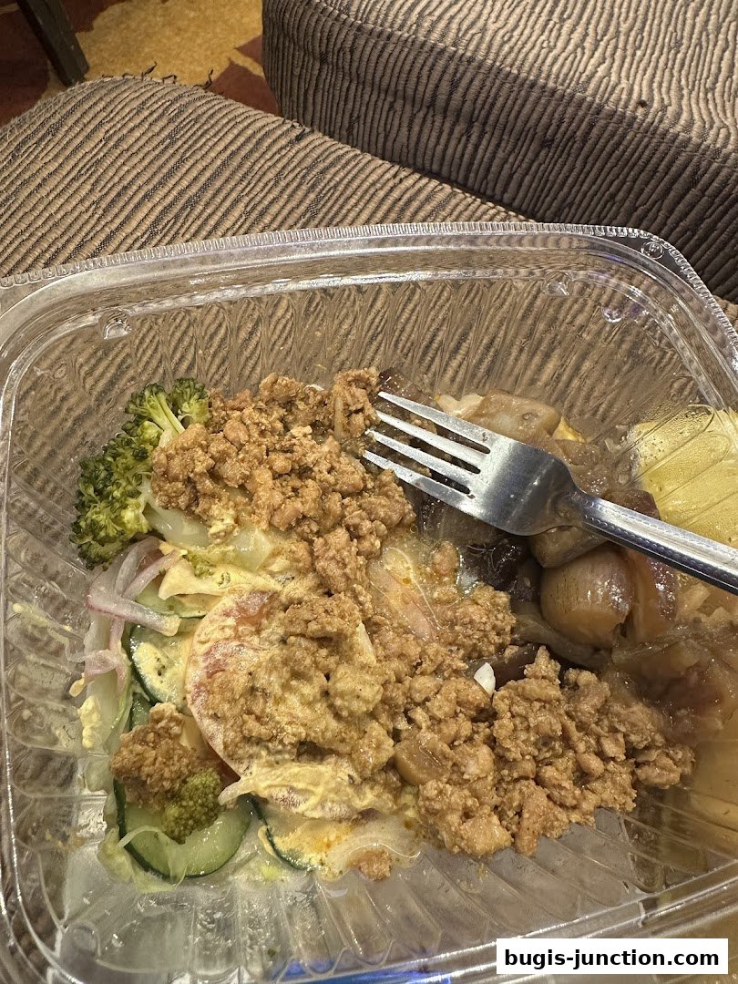A clear plastic container filled with a meal, featuring minced meat, vegetables, and a fork.