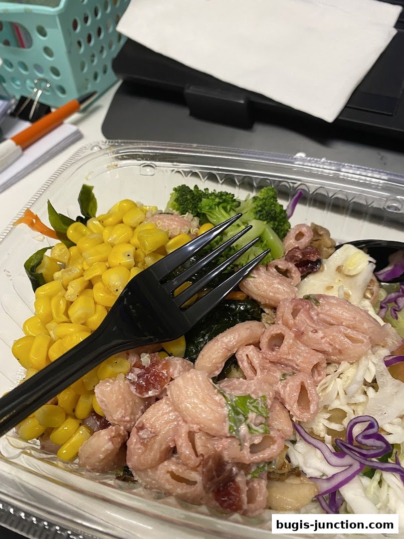 A close-up of a takeout salad with pasta, corn, broccoli, and cabbage.