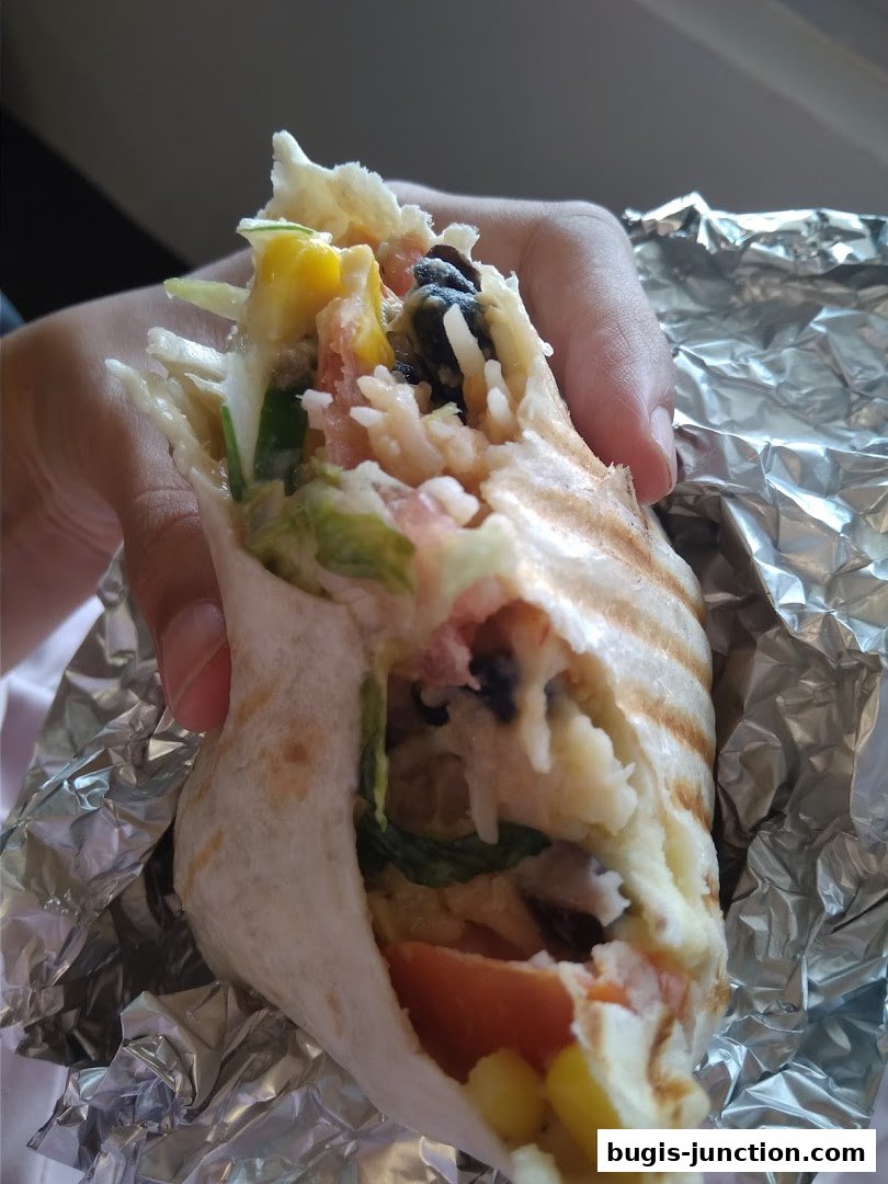 A hand holds a delicious burrito filled with rice, beans, corn, and vegetables.