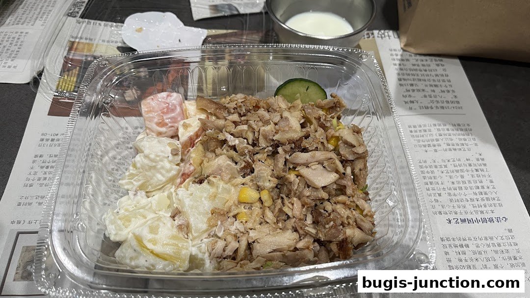 A takeaway container filled with a salad featuring shredded chicken, corn, and potato salad.
