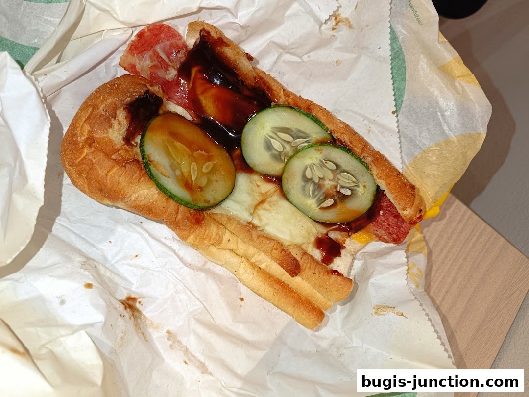 A Subway sandwich with cucumber slices, sauce, and meat on a white paper wrapper.