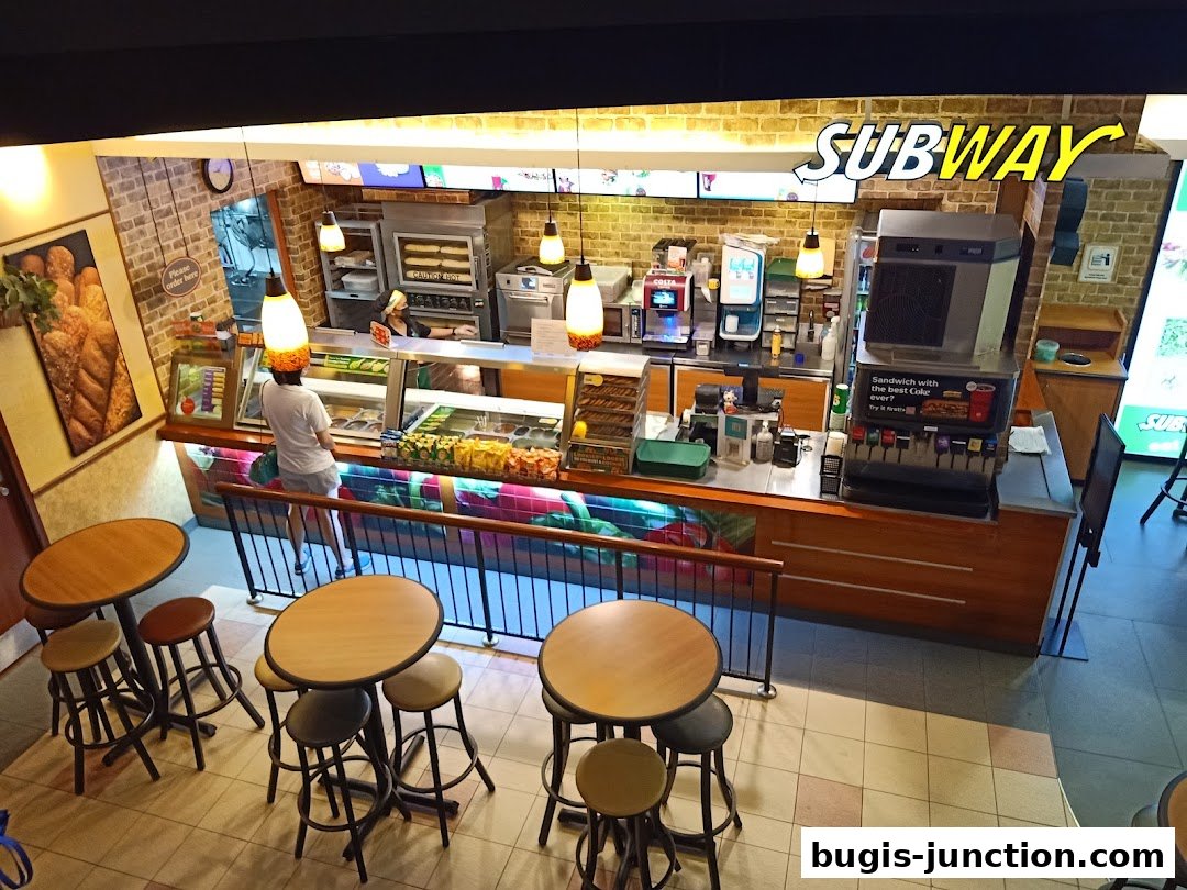An interior view of a Subway restaurant showing the counter, seating, and food preparation area.