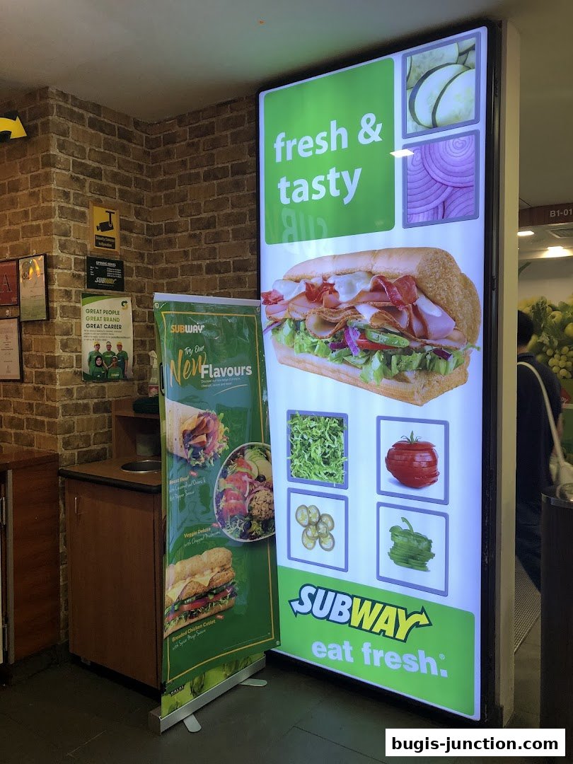 A Subway shop with a large illuminated sign showcasing a sandwich and fresh ingredients.