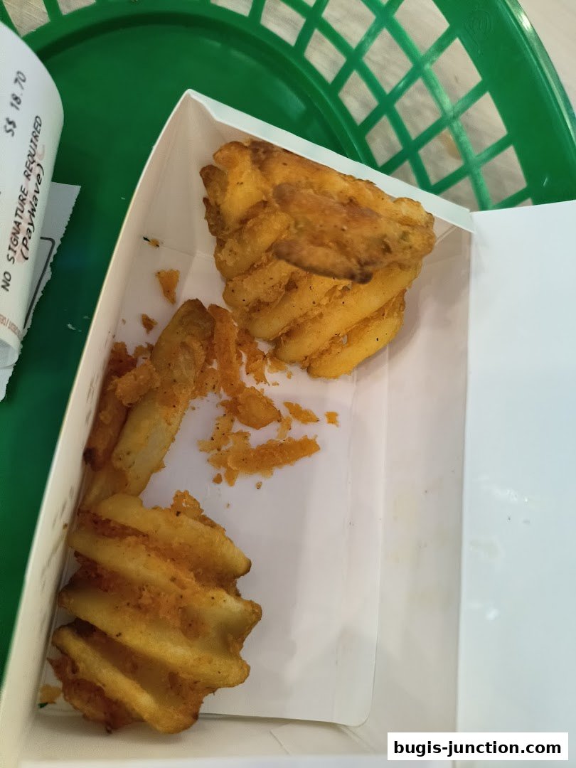 A box of seasoned waffle fries sits in a green basket, with a receipt visible.