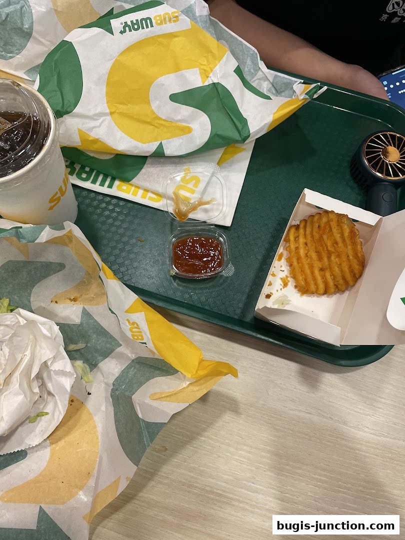 A tray with Subway sandwiches, a drink, dipping sauce, and waffle fries.