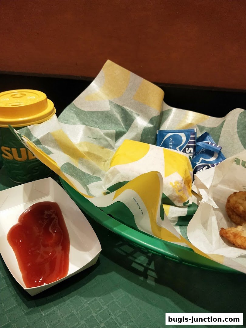 A Subway meal featuring a sandwich, hash browns, ketchup, and a drink.