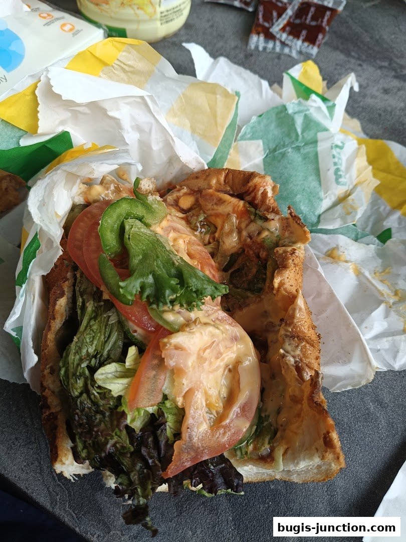 A Subway sandwich with fresh vegetables and sauce, wrapped in paper.