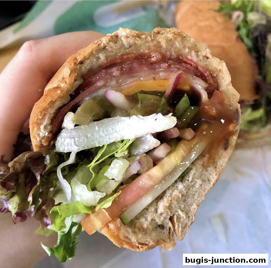 A hand holds a delicious, fully-loaded Subway sandwich with fresh vegetables and meat.