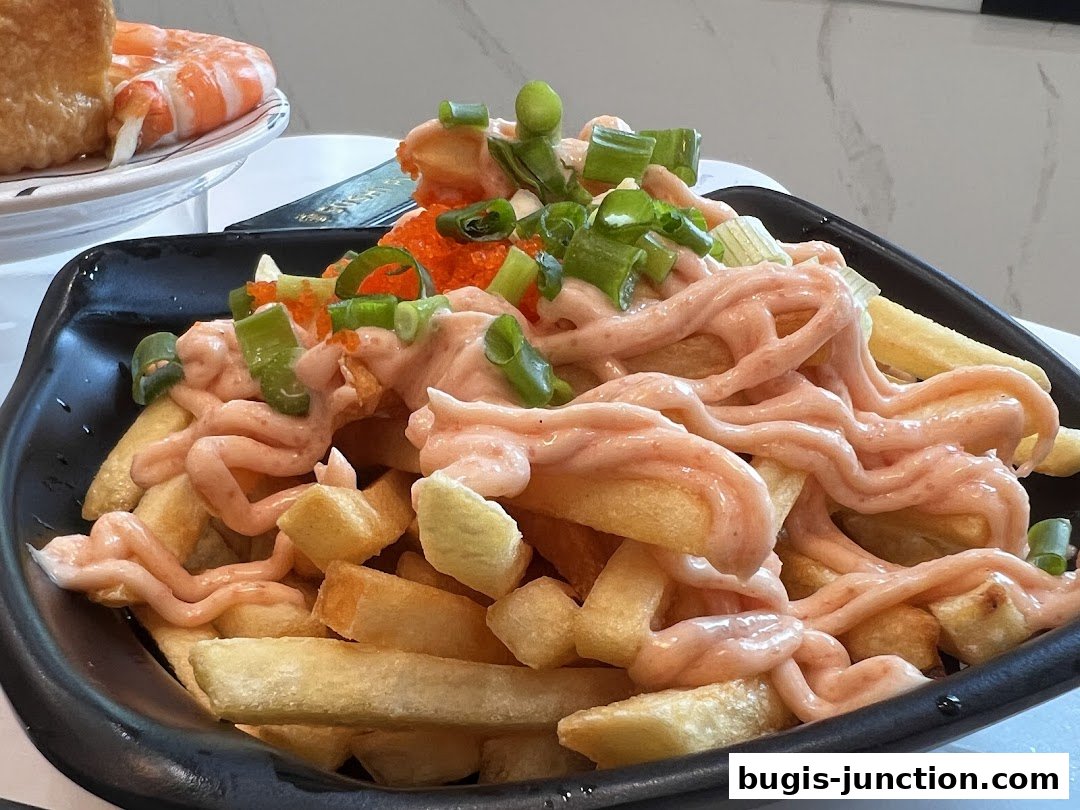 A close-up of a black bowl filled with crispy fries topped with pink sauce, green onions, and roe.