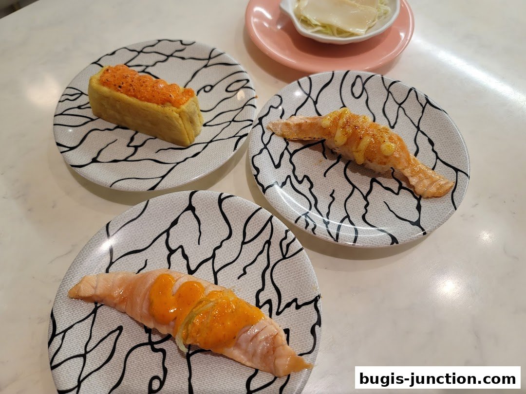 Three plates of sushi and a small dish of mayonnaise are arranged on a white table.