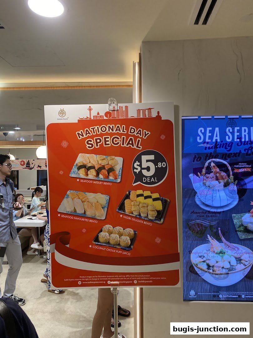 A sign advertising a National Day Special deal for Sushi Plus, featuring various bento boxes and a dessert.