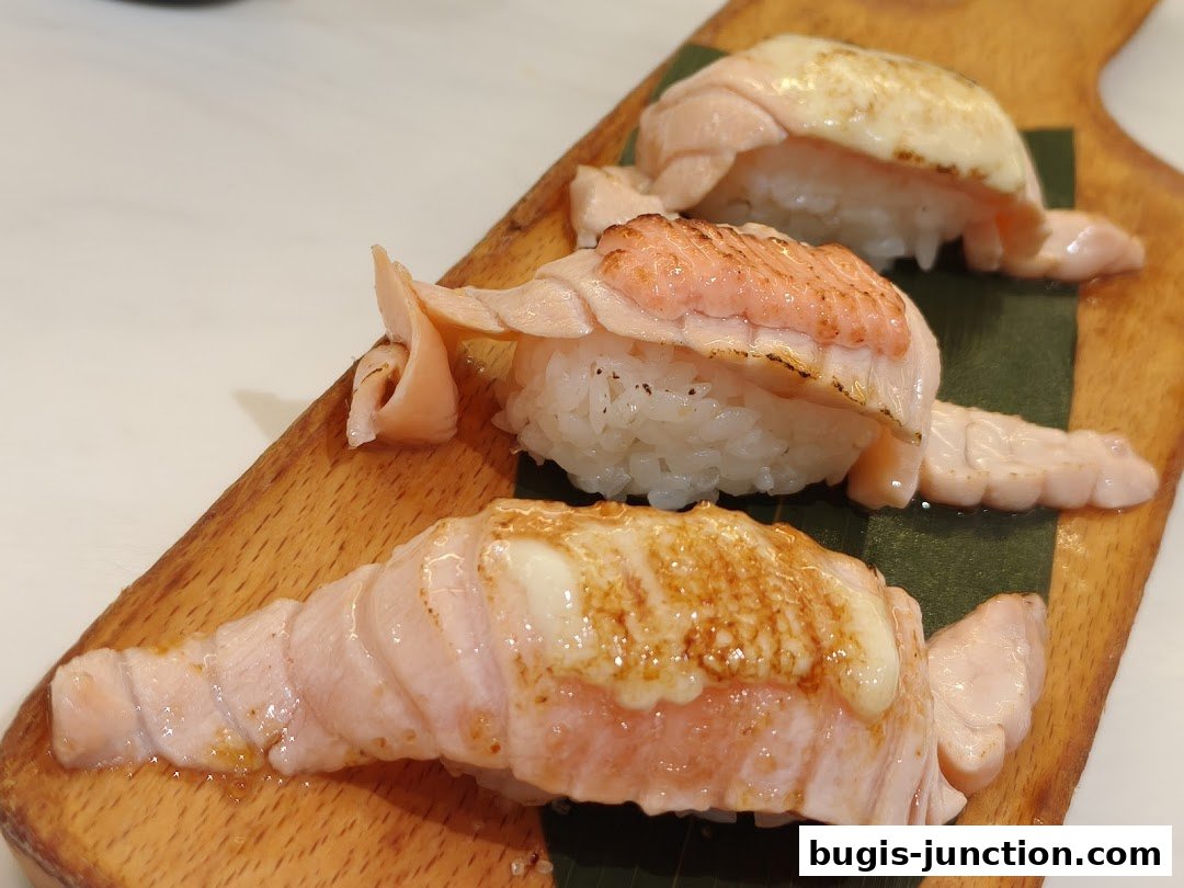 Three pieces of salmon sushi with torched toppings on a wooden board.