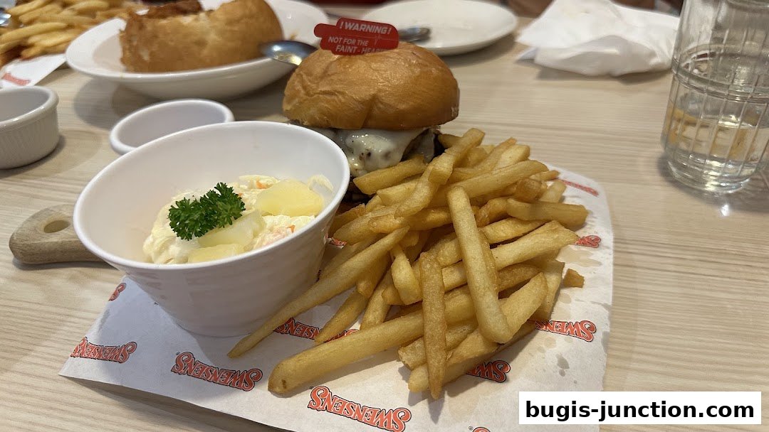 A close-up of a Swensen's burger with fries and coleslaw, served on branded paper.