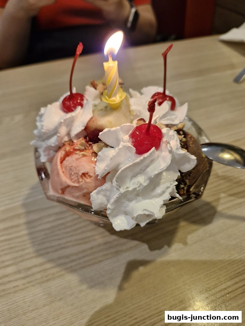 A festive ice cream sundae with a lit birthday candle and cherries.