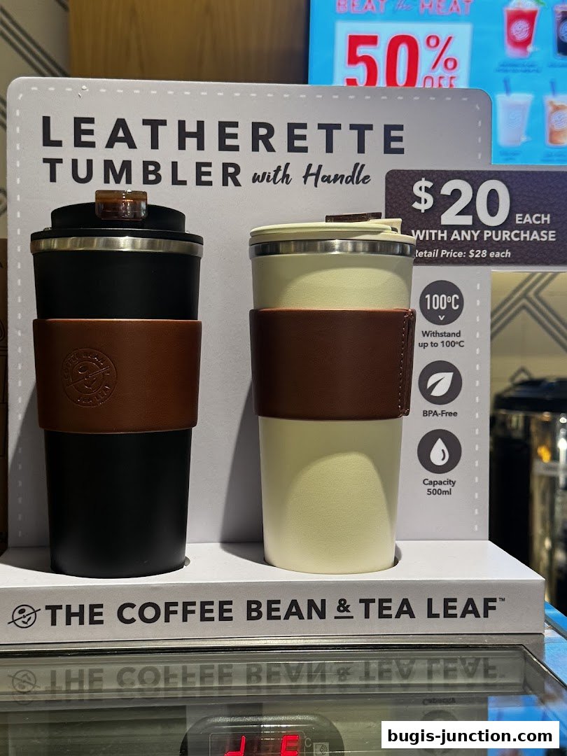 Two leatherette tumblers with handles, one black and one cream, displayed with promotional signage.