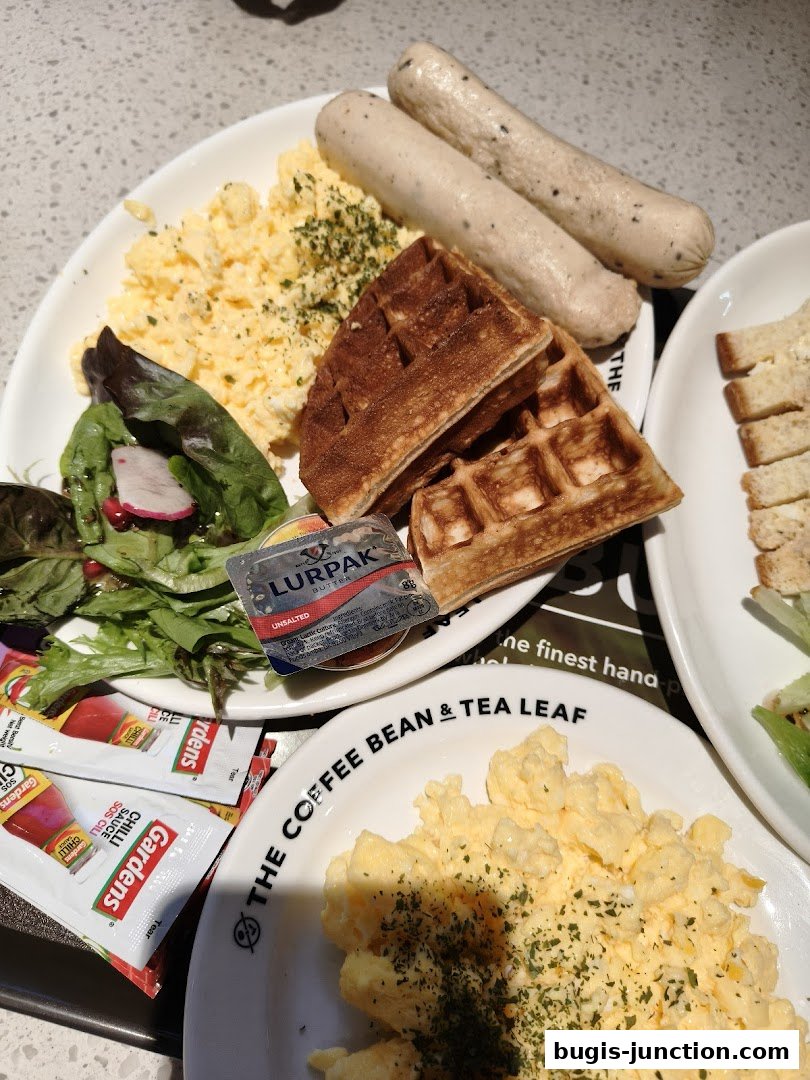 A close-up of a breakfast plate with scrambled eggs, sausages, waffles, and salad.