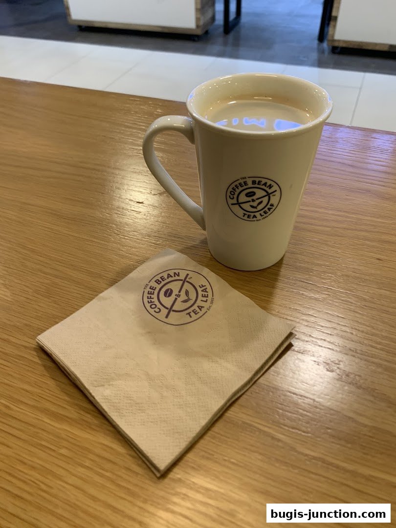 A white mug of coffee sits on a wooden table next to a folded napkin.