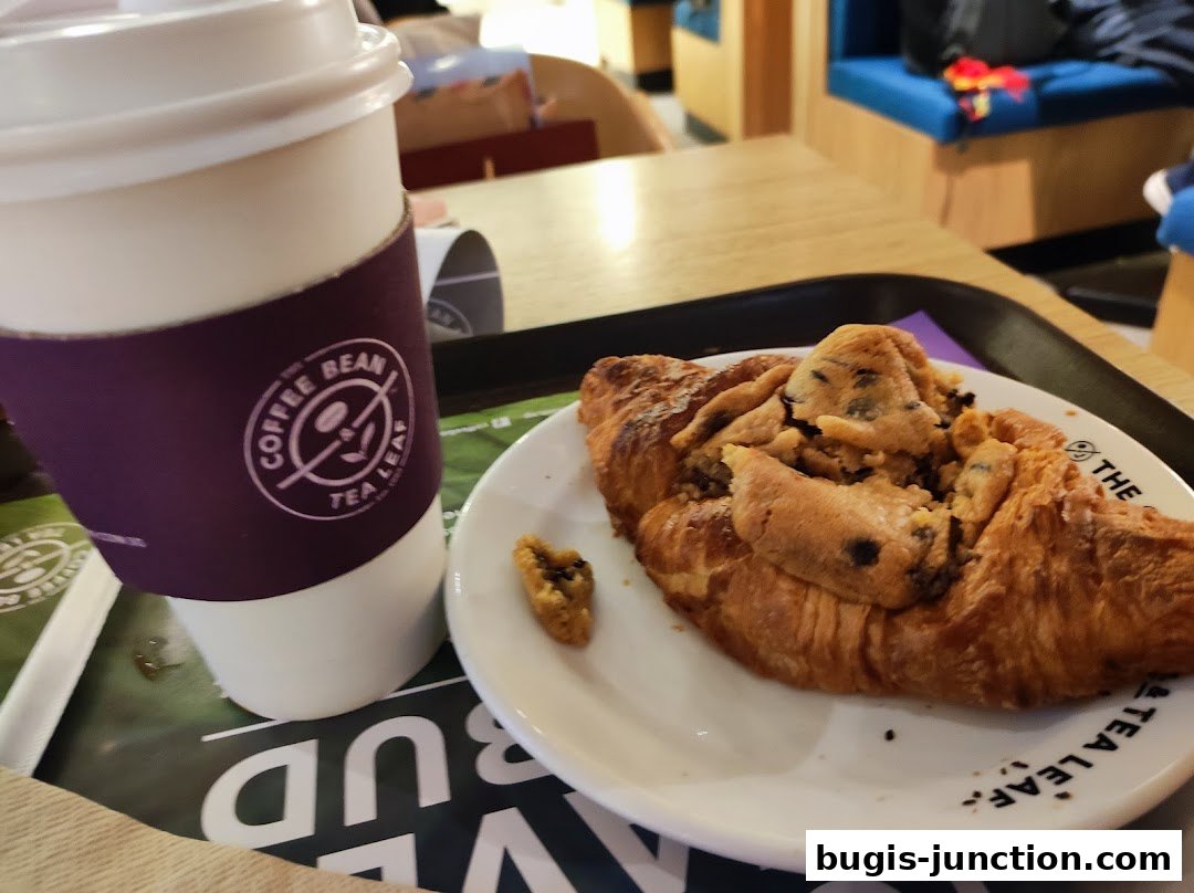 A coffee cup and a croissant with chocolate chips on a tray at The Coffee Bean and Tea Leaf.