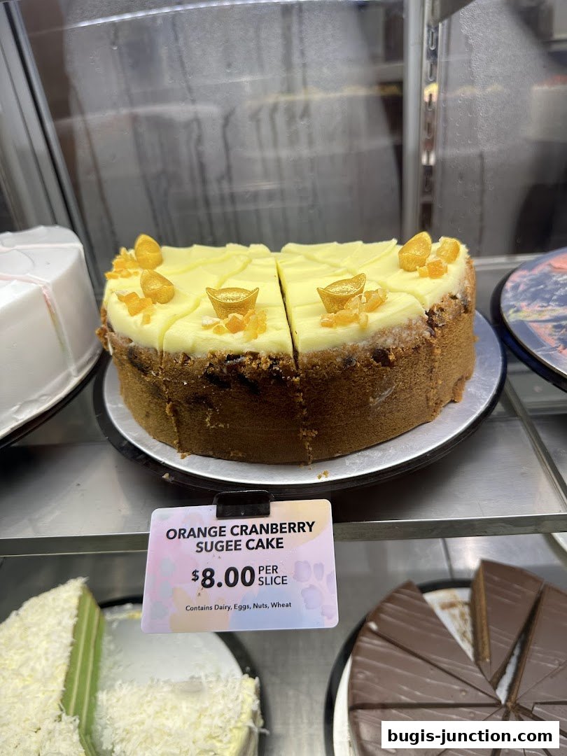 A slice of orange cranberry sugee cake with frosting and candied orange peel.
