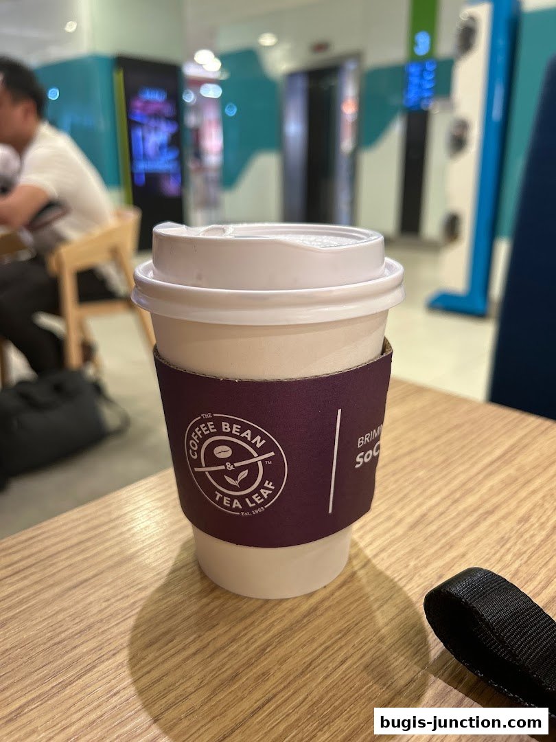 A close-up of a Coffee Bean and Tea Leaf branded cup with a sleeve on a wooden table.