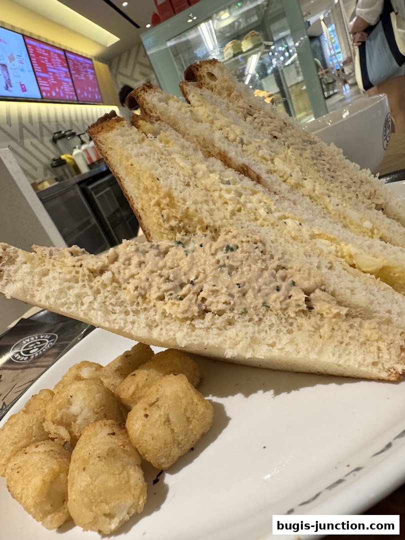 A close-up of a tuna sandwich with tater tots on a white plate.