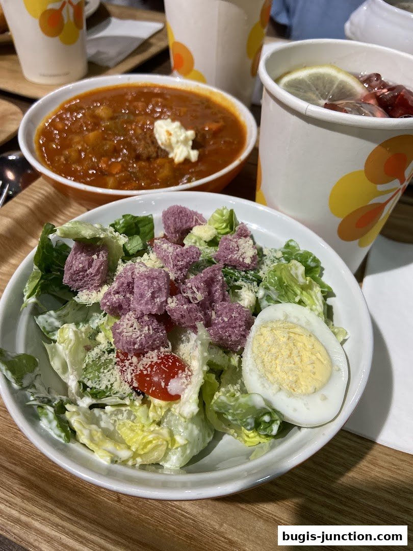 A close-up of a salad and a bowl of soup with drinks from The Soup Spoon.