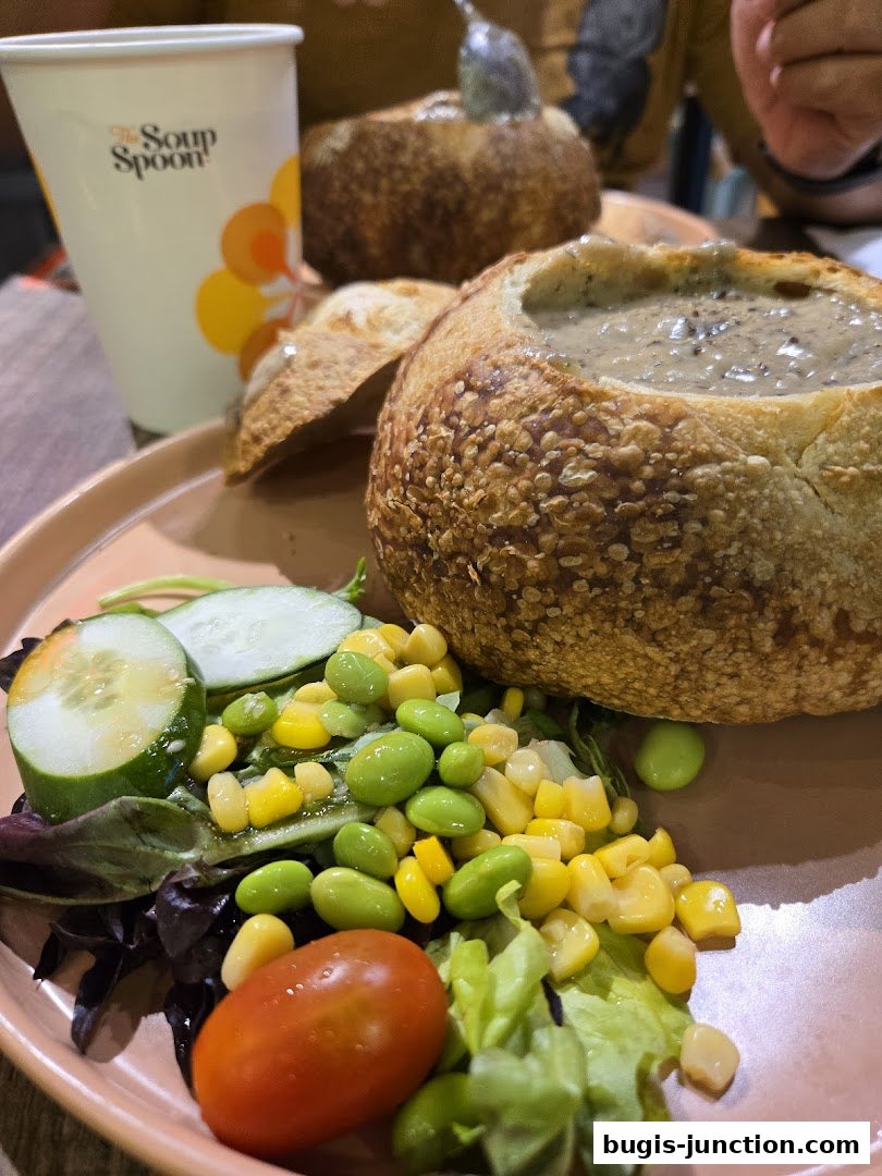 A close-up of a bread bowl filled with soup, served with a side salad and a drink cup.