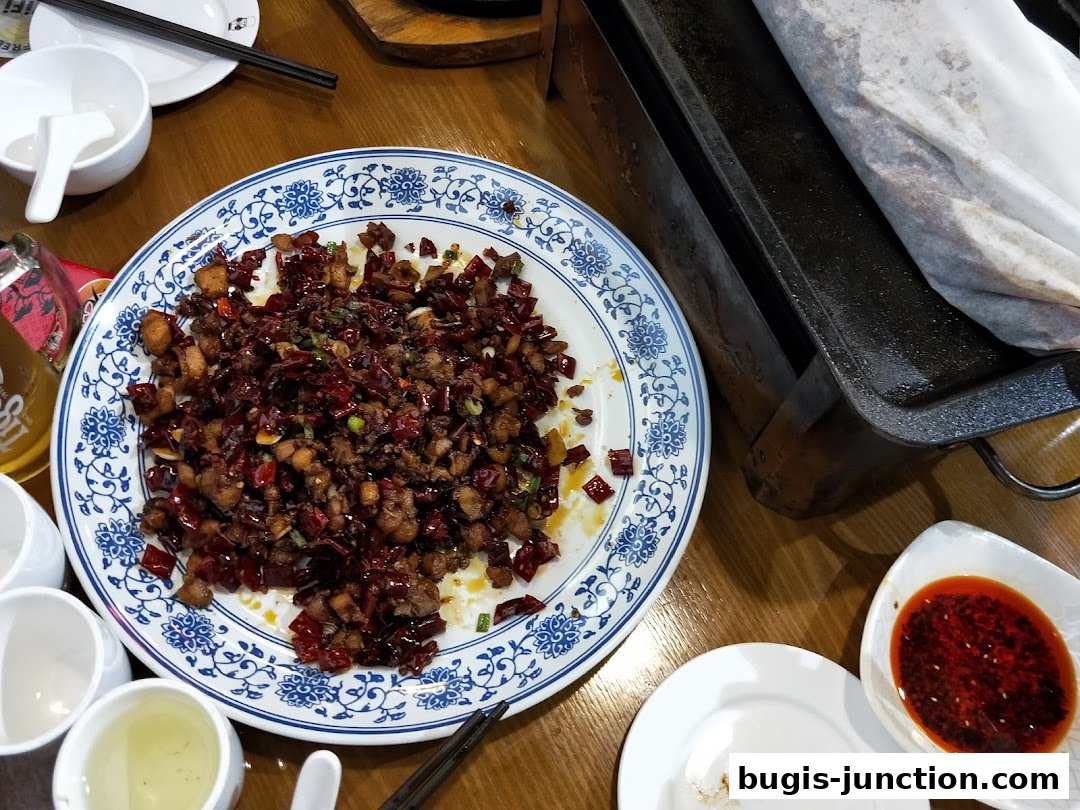 A plate of spicy fried chicken with chili peppers and a side of dipping sauce.