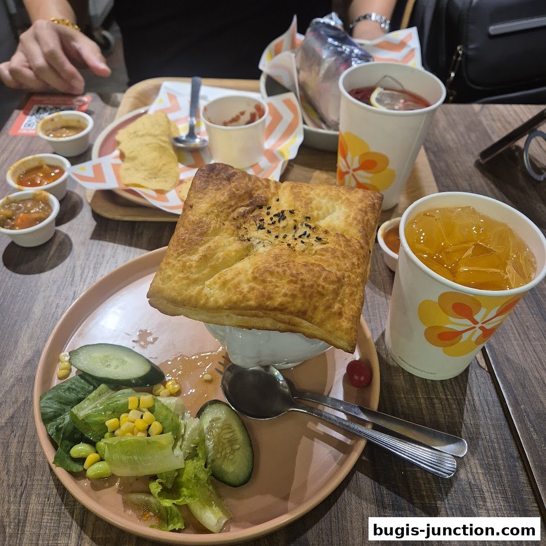 A delicious meal featuring a pastry-topped soup, salad, chips, and drinks.