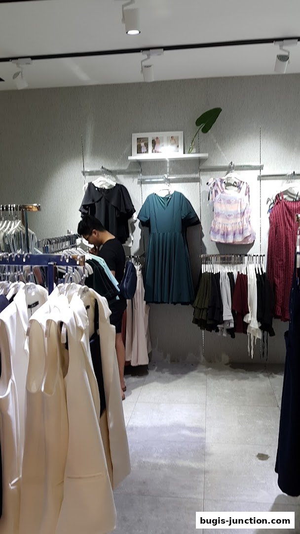 A person browses through a well-lit clothing store with racks of dresses and jackets.
