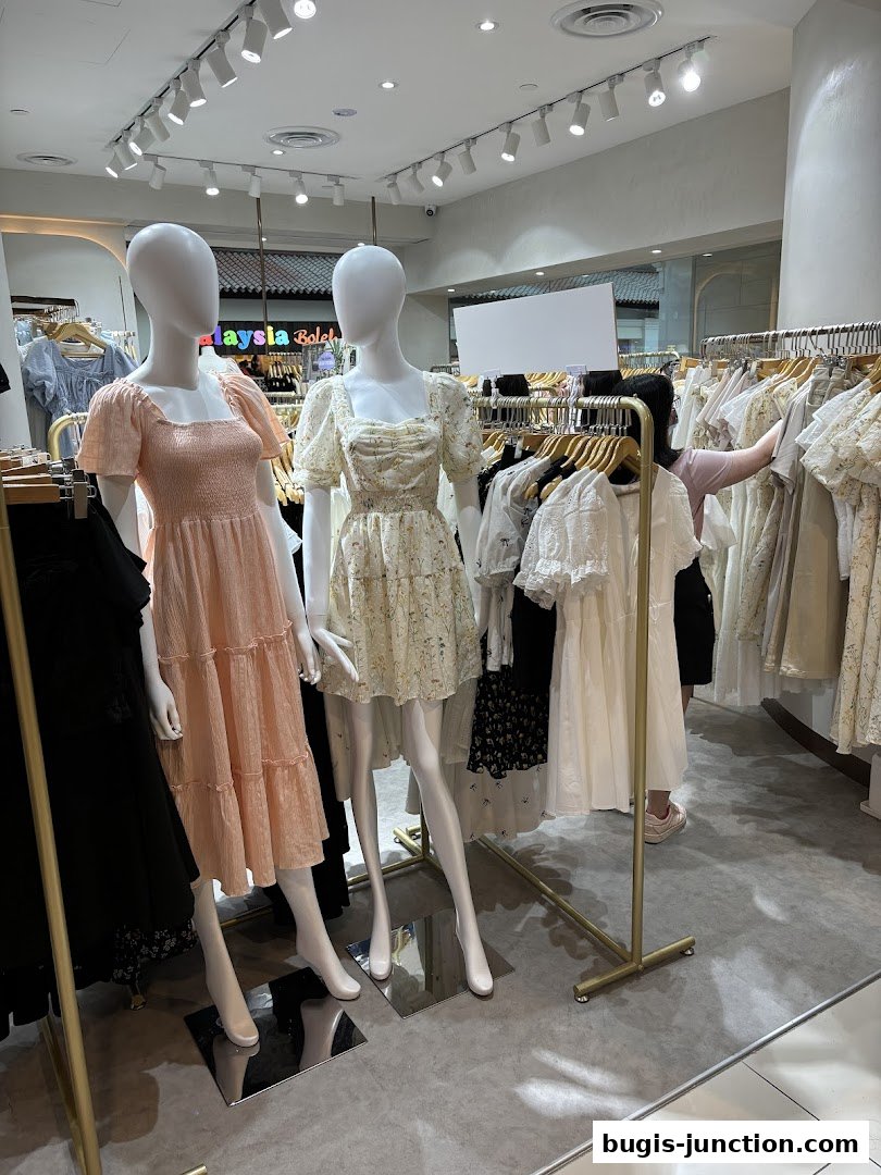 Mannequins display dresses in a clothing store with racks of apparel in the background.