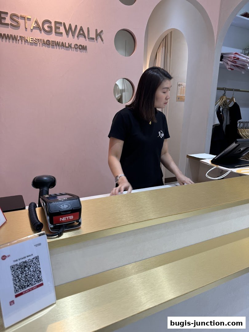A shop assistant stands behind a counter at The Stage Walk, with the shop's logo visible.