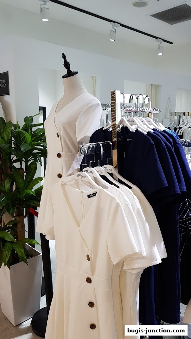 Mannequin and dresses displayed on hangers in a brightly lit retail store.