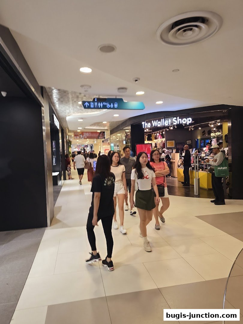People walking in a mall hallway towards a shop called 'The Wallet Shop'.