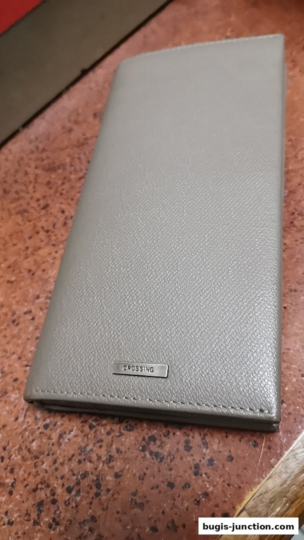 A close-up shot of a grey leather wallet with the brand name 'CROSSING' embossed on a metal plate.