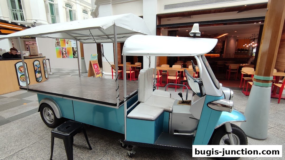 A blue and white tuk-tuk style cart with a canopy parked in front of a restaurant.
