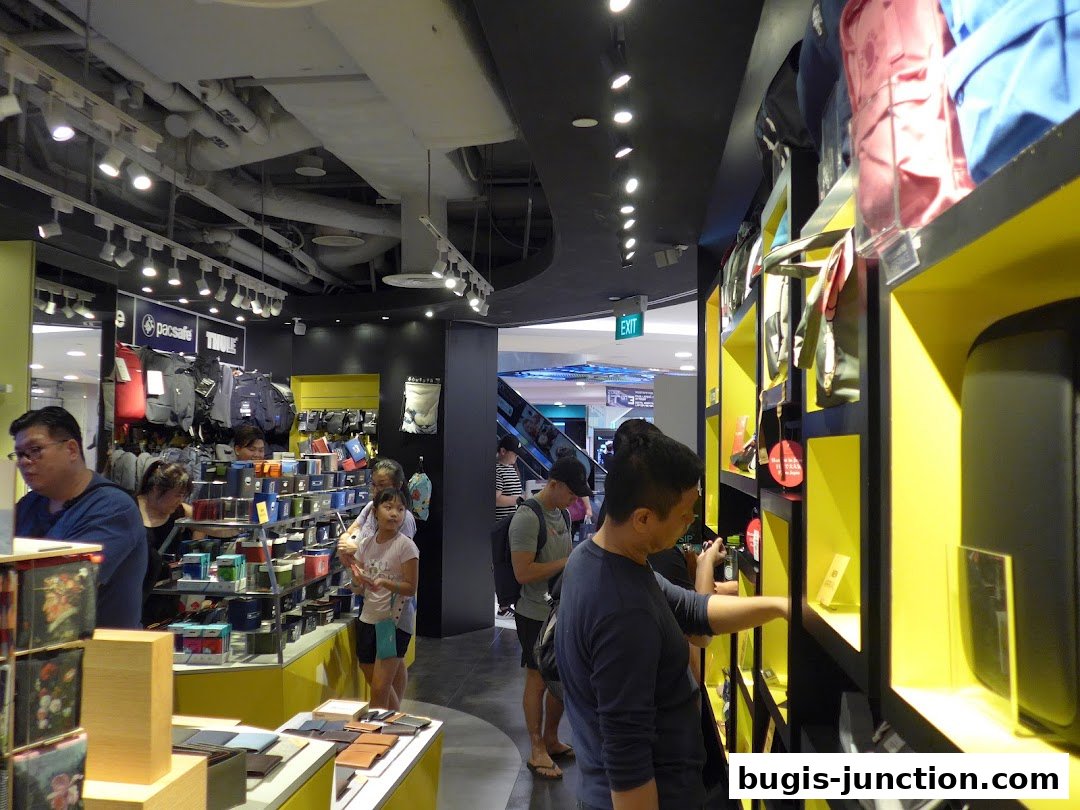 Customers browse a well-lit retail store displaying wallets, bags, and travel accessories.
