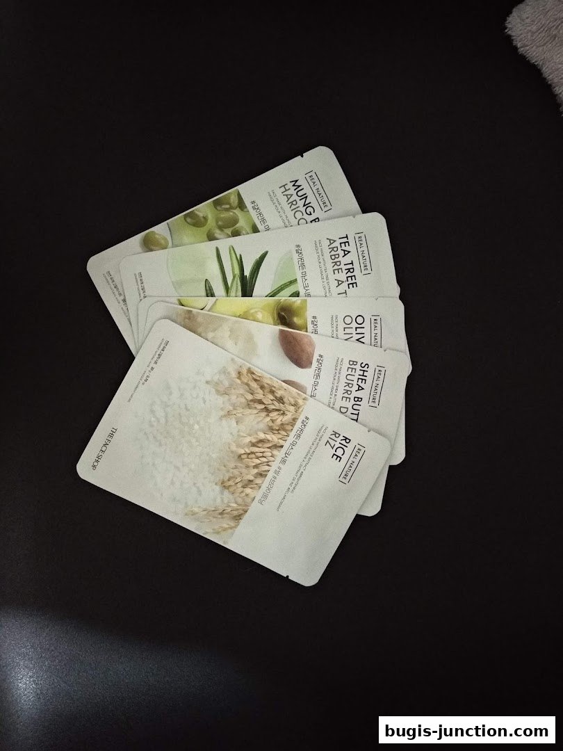 Several face masks from THEFACESHOP's Real Nature line are fanned out on a dark surface.