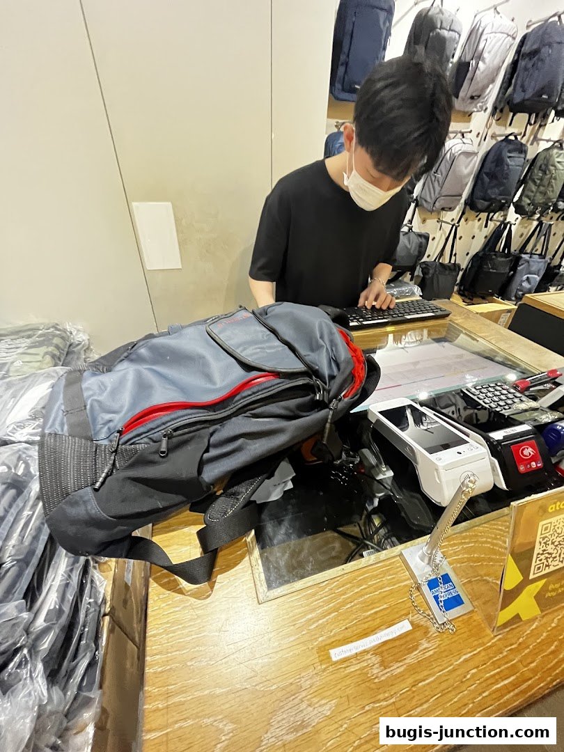 A store employee wearing a mask assists a customer at a checkout counter with bags.