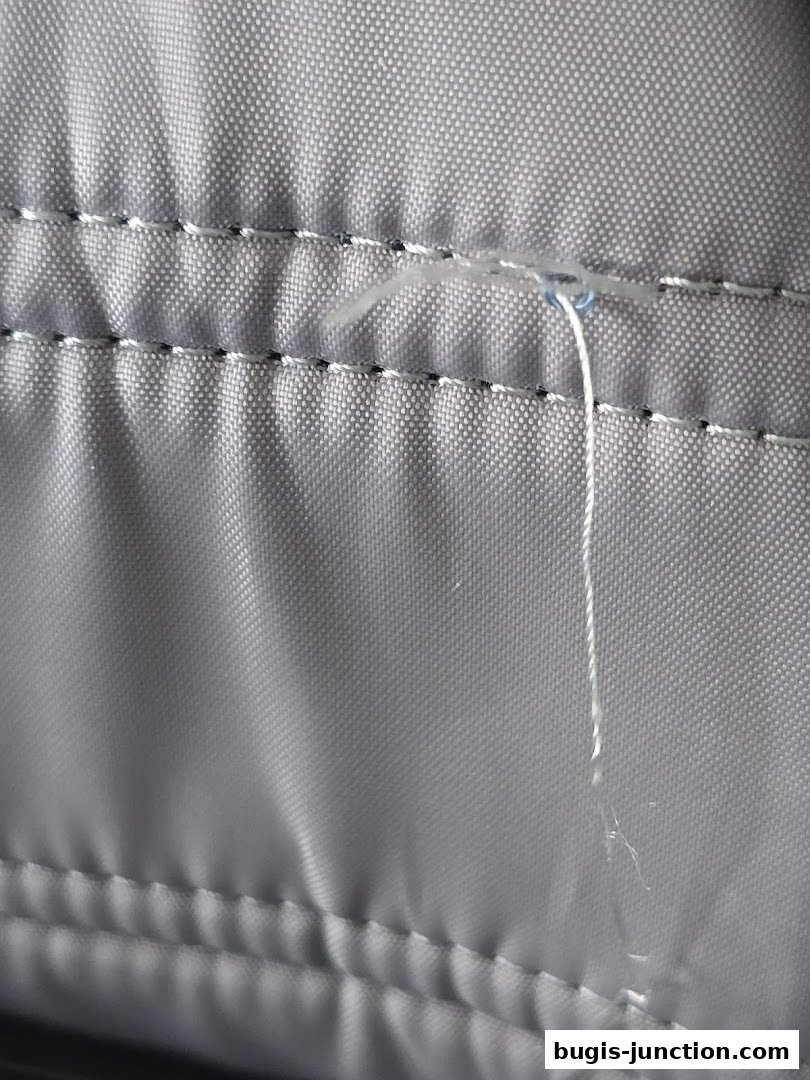 Close-up of grey fabric with stitching and a loose thread.