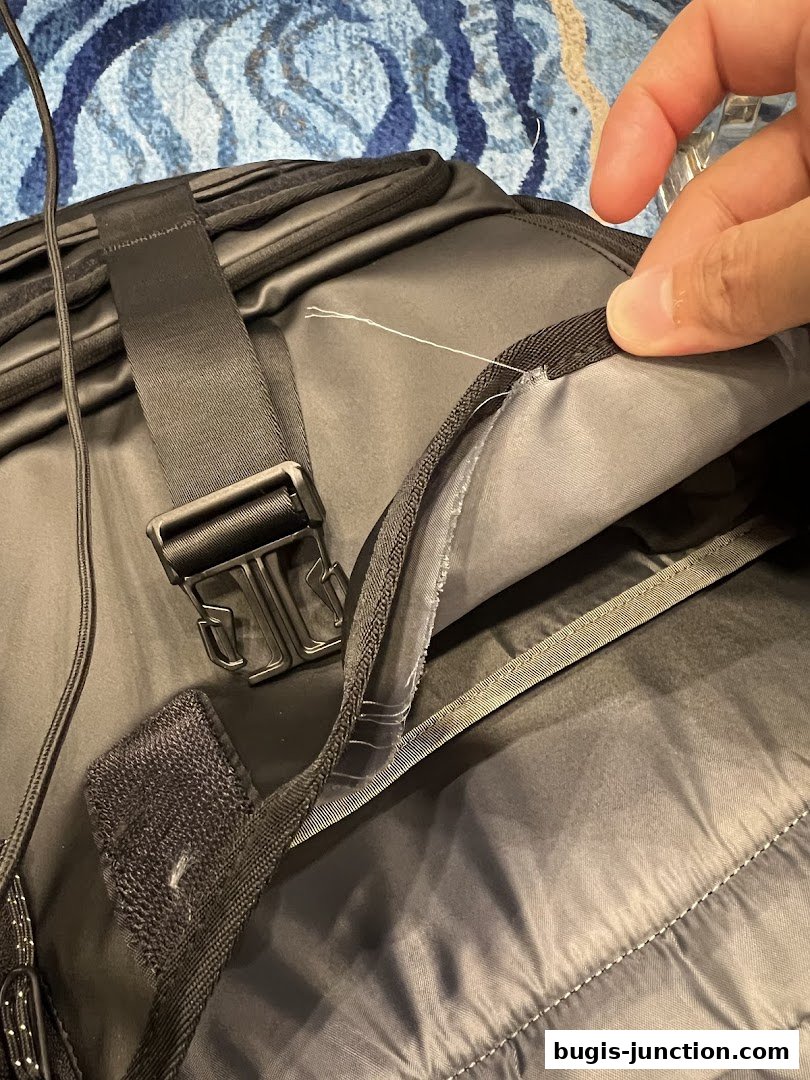 A close-up of a black Timbuk2 backpack, showing stitching and a hand inspecting the interior.